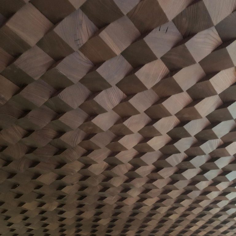 Das Bild zeigt eine Saunadecke, die aus kleinen, dunkelbraunen Holzklötzen besteht. Die Muster erzeugen einen 3D-Effekt und sehen besonders 